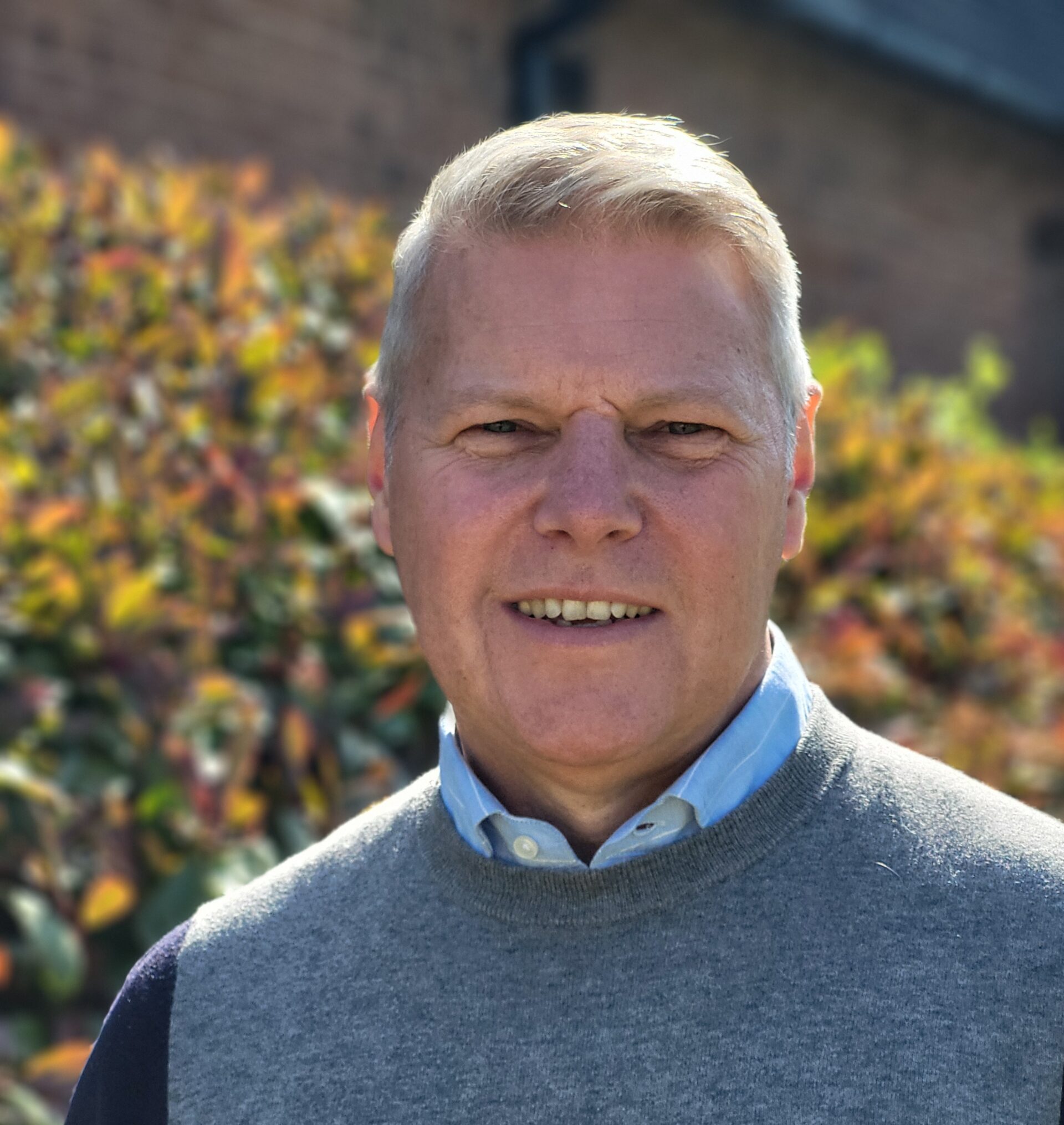 Portrait of Ian Bullock, new CEO of Eternal Wall of Answered Prayer, standing outdoors in front of autumnal foliage.